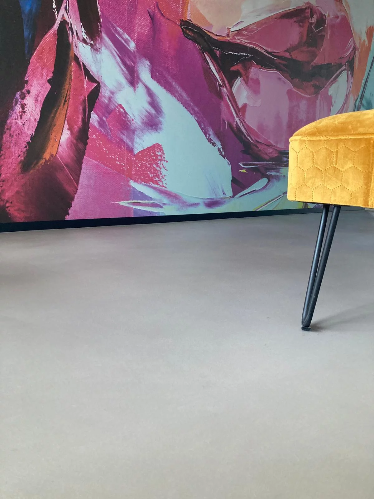 abstrakcyjna kolorowa ściana z nowoczesnym żółtym fotelem i jasną posadzką z mikrocementu na podłodze